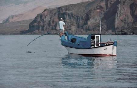 pescador en pequeña embarcación capturando a caña